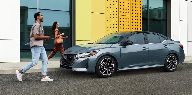 A man and woman walking toward a grey 2024 Nissan Sentra.