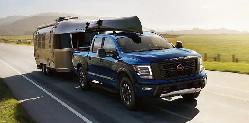A 2024 NIssan Titan towing a airstream camper behind it with a canoe on the roof.