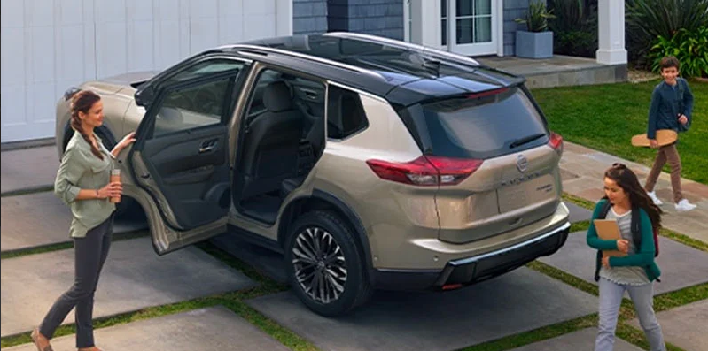 A woman closing the rear drivers side door of a 2025 Nissan Rogue parked in their driveway.