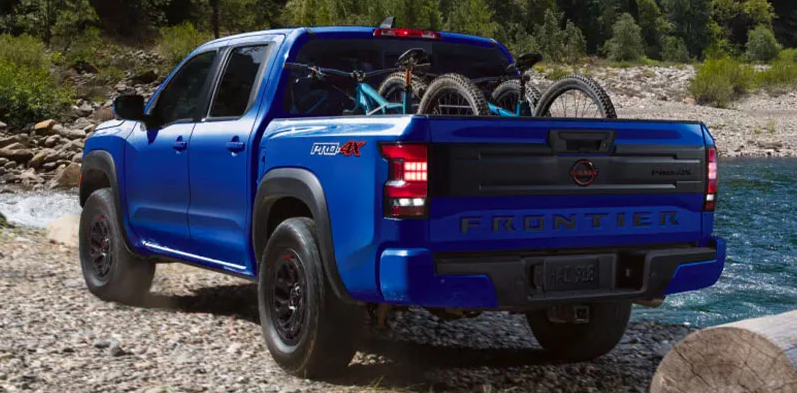 A blue 2025 Nissan Frontier parker on the edge of a river with bikes in the back.