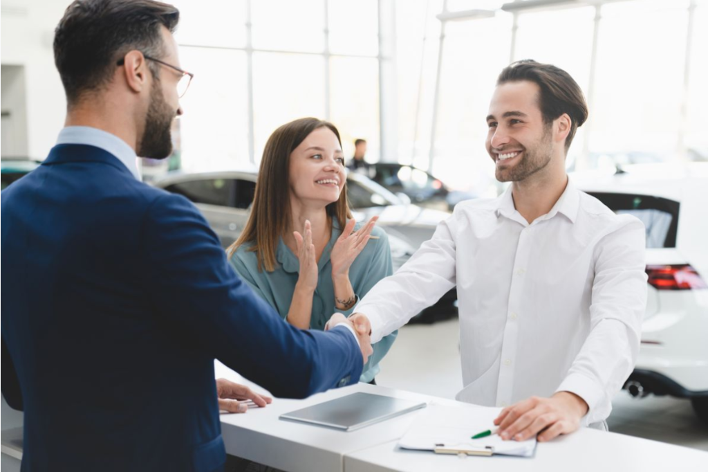 2 Individuals shaking hands over the counter of a Nissan dealership.