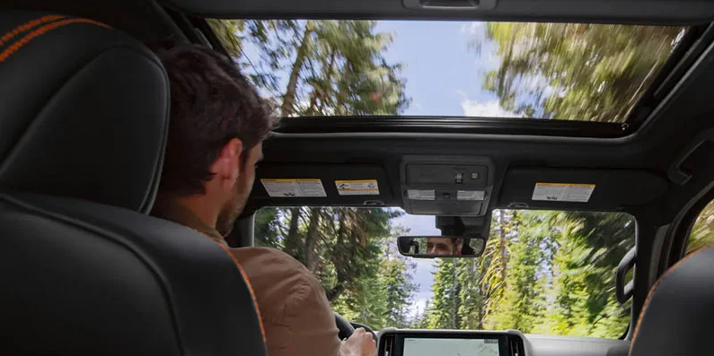 A man driving a 2025 Nissan Frontier down a tree lined road.