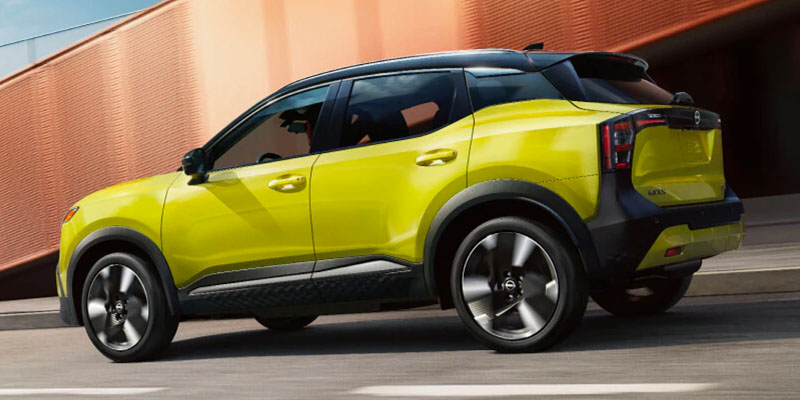 2026 Nissan Kicks compact SUV in bright yellow driving along a city street, featuring a sporty design, black roof accents, and modern rear styling.