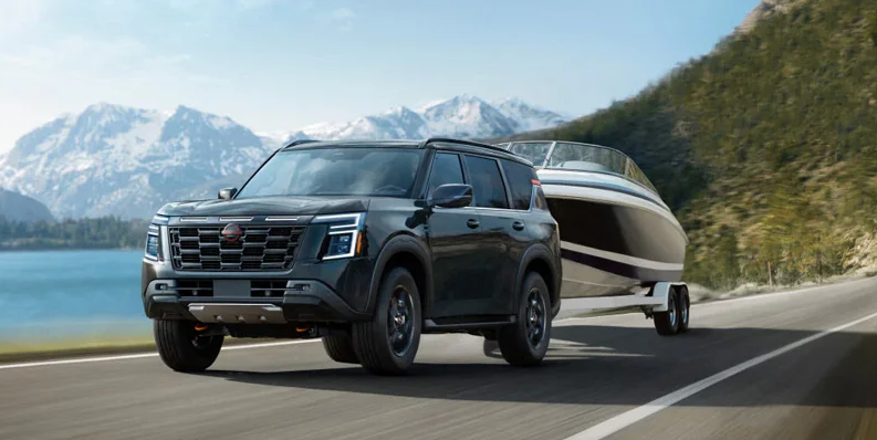 A green 2026 Nissan Armada towing a boat down the road.